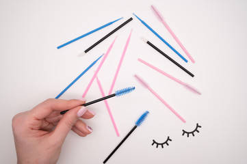 Top view of flatlay from eyelash extension tools. Female hand holds colored brushes for combing cilia.