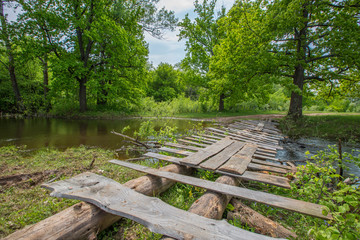 Fototapeta premium homemade bridge made of logs and boards through the forest channel