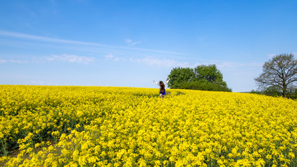 young woman running in a field with yellow flowers, blue sky, space