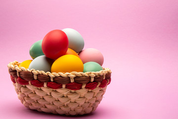 Fototapeta na wymiar Multicolored Easter eggs in a basket on rose background