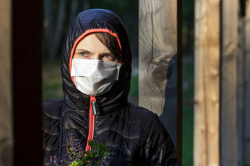 Portrait of a sad young woman in a medical mask on her face and a hood in nature alone