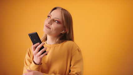 Naklejka premium Young caucasian girl listening to the music on her smartphone on the wireless headphones. Isolated on the orange background. Copy space