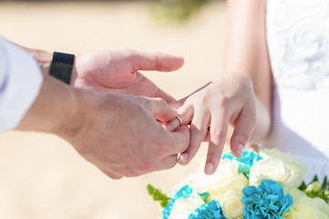 Bride and groom exchanging wedding rings close up during symbolic nautical decor destination wedding marriage on sandy beach in front of the ocean in Punta Cana, Dominican republic 