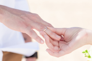 Bride and groom exchanging wedding rings close up during symbolic nautical decor destination wedding marriage on sandy beach in front of the ocean in Punta Cana, Dominican republic 