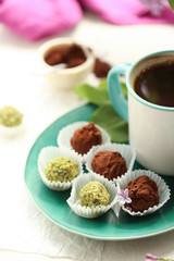 On a white background is a cup with a coffee, on a turquoise plate of candy and truffle, and in a vase is a lilac.
