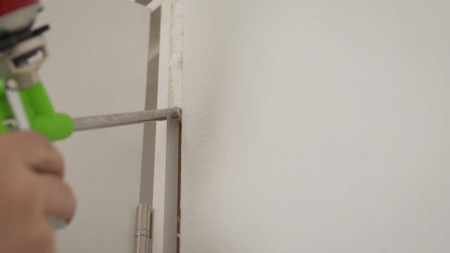 the master with the help of mounting foam, repairs the door jamb. The master uses construction foam. young man sets the door. The installer fills the door slope with foam