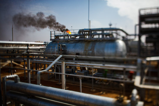 Burning gas torch on oil refinery plant in the yellow desert. Ecology concept. Partially blurred tilt-shift photo.