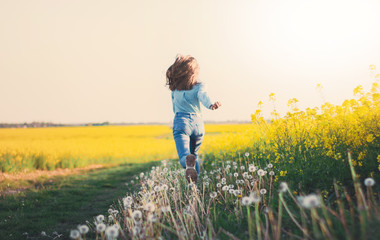 Happy Teenager Girl in Blue Jeans and White Shirt Running through Rapeseed field and on Dandelions. Lifestyle concept 