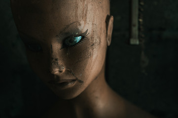 Close-up portrait of an old plastic doll from a shop window standing in a dirty garage