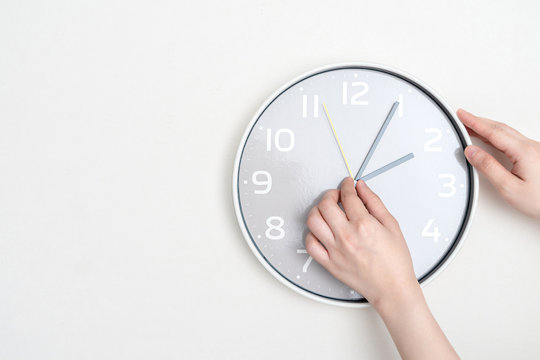 Woman hand changing time on white clock. Time change concept and punctuality.