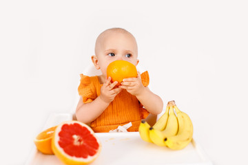 baby girl sitting in a child's chair eating fruit on a white background. baby food concept, space for text