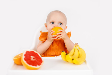 baby girl sitting in a child's chair eating fruit on a white background. baby food concept, space for text