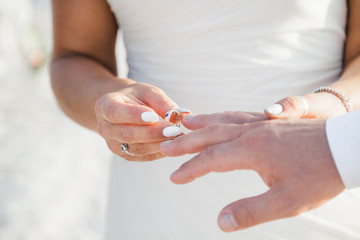 Bride and groom exchanging wedding rings close up during symbolic nautical decor destination wedding marriage on sandy beach in front of the ocean in Punta Cana, Dominican republic 