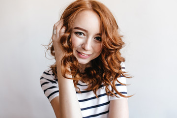 Fototapeta premium Ecstatic girl wears ring touching her ginger hair. Indoor portrait of inspired female model in casual outfit isolated on white background.