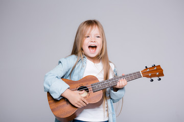 The girl sings and plays the ukulele. The child laughs, poses for the camera and enjoys the music
