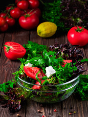 Cup with a salad of red tomatoes, feta cheese, olive oil and herbs. Healthy and wholesome food, fresh vegetable salad. Close-up, wooden background