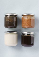 Vegan organic paste of flax seeds, milk thistle, peanuts and coconut in glass jars on light blue background, urbech, Vertical format, Top view