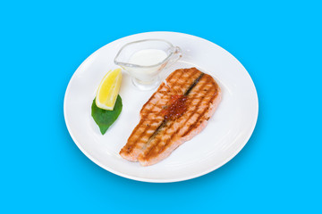 Grilled salmon with caviar, lemon and cream sauce isolated on blue background