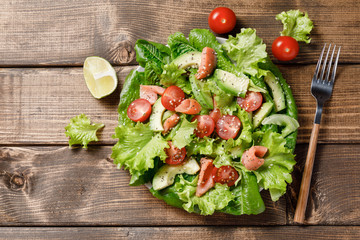 Salmon salad with avocado, green leaves and tomatoes on wooden table