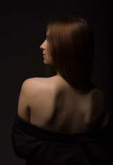 Portrait of a young woman with a bare back at studio. Back view.
