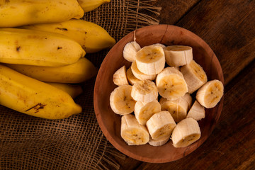 A banch of bananas and a sliced banana on wood background.