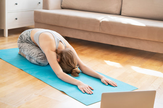 Young attractive women doing yoga exercise at home, Balasana, Child Pose, Ardha-Kurmasana Half Tortoise Pose in livingroom. Working out wearing sportswear bra and pants. Healthcare concept