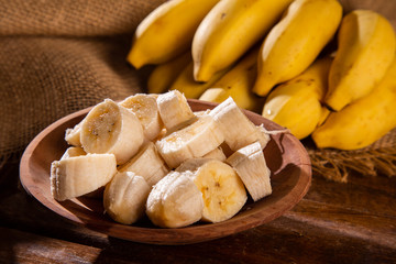 A banch of bananas and a sliced banana on wood background.