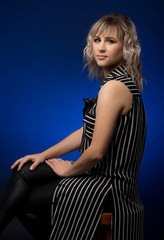 Fototapeta na wymiar Beautiful girl in the studio on a dark blue background in a dress or sundress sits on a red chair