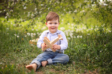 Little cute blond boy playing with a wooden plane in the summer park on the grass on a sunny day, focus on the child, blurred background