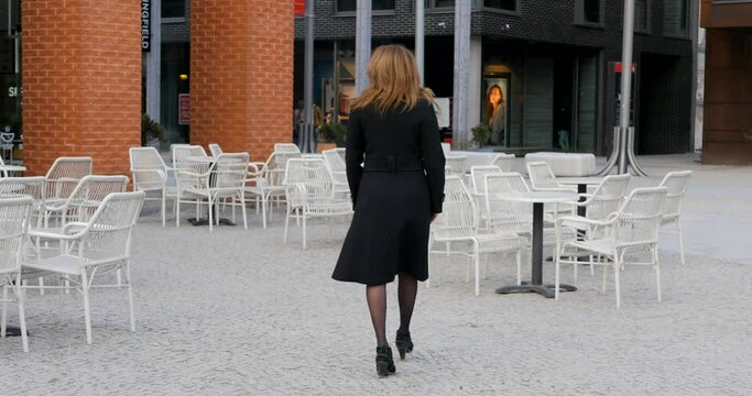 Young woman in casual black coat sits in outdoor cafe. Nobody else oytdoors. Spring time