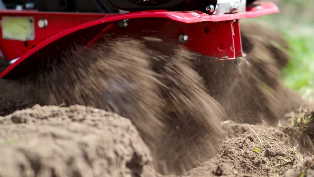 Tiller engine working in garden in 4K VIDEO. Cultivator machine cultivating field at spring. Extreme close-up of soil throwing away of blades. Modern farming, technology agriculture. Close-up.