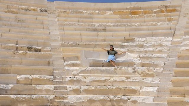 Young pretty girl tourist sitting on the throne in an ancient greek theater