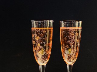Two flute glasses of sparkling rose wine against a black background. No people. space for copy.