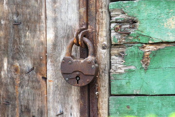 A old iron padlock hangs on the wood door. Locked door to the premise. Concept of protection, incarceration, protection, prison.