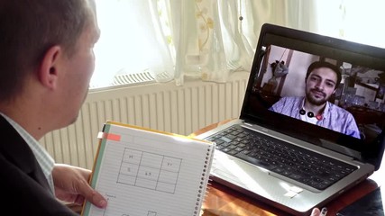 Middle aged man taking notes in a video call he's having with younger colleague - Powered by Adobe