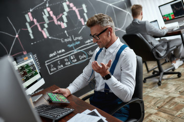 Finding More Possibilities. Stylish businessman, trader using his tablet pc, while sitting by desk...