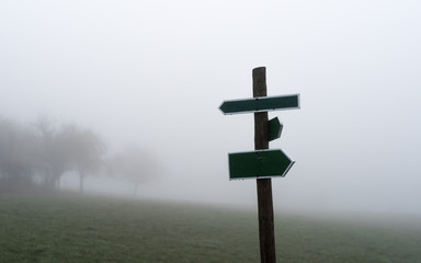 Two opposite arrows on a wooden pole with meadow and fog