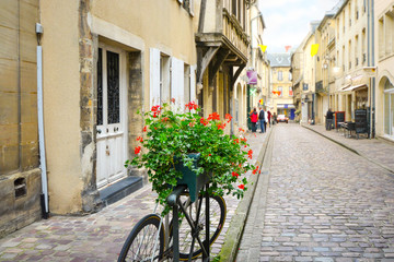 Fototapeta na wymiar A bicycle is parked by a planter flower box with blurred background on a picturesque street in the Medieval village of Bayeux France in Normandy.