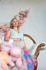 beautiful glamour pregnant woman in a colorful puffy dress is sitting on sofa in a floral loft studio. Happy pregnancy