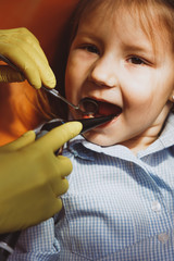 Crop dentist in yellow gloves checking teeth of cheerful little girl during appointment in contemporary clinic