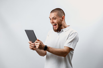 Portrait of a handsome happy bearded man in a white T-shirt with a tablet on a white background. isolated, emotions
