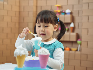 toddler girl pretend play food preparing role against cardboard blocks kitchen background