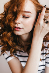 Close-up portrait of sensual ginger lady with brown makeup. Indoor photo of glad female model playing with her red wavy hair.