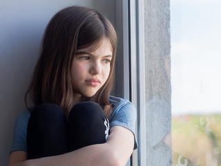 a lonely girl sits by the window and looks sadly at the street