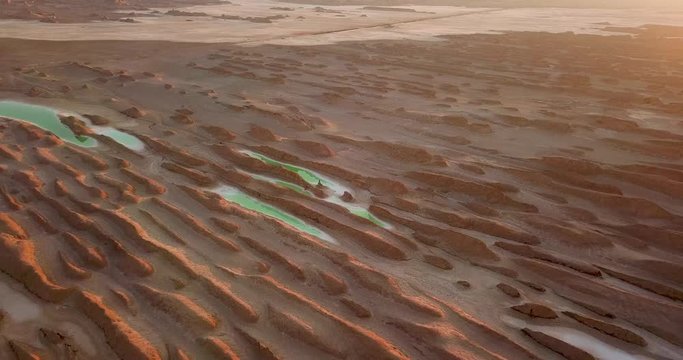 Sunset glow in aerial shot from beautiful gold desert pattern and green rainwater salt lake