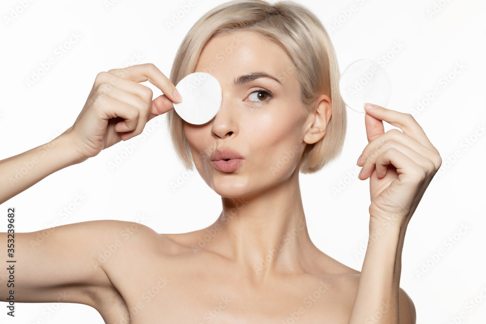 Wall mural Woman covering eye with cotton pad with lips folded  and holding other in hand looking aside. 