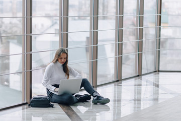 attractive girl working with laptop and things in airport terminal or office on floor. travel atmosphere or alternative work atmosphere. freelancer student travels to business meeting. 