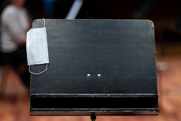 A black music stand with a face mask hanging on it representing performance restrictions during a...