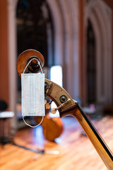 A face mask hanging from the scroll of an acoustic double bass on stage representing performance...