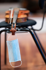 A face mask haning from the scroll of an acoustic violin or viola that is on a chair representing performance restrictions during a pandemic